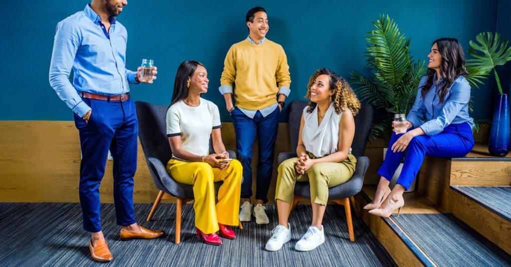 A diverse group of five professionals engaging in a casual indoor meeting, smiling and talking.