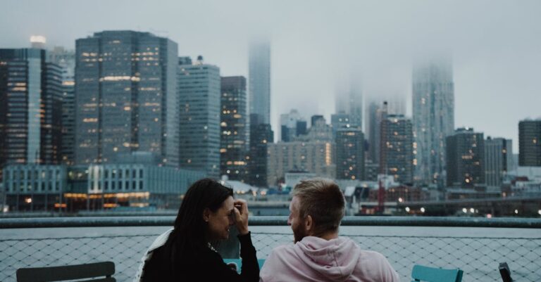A couple enjoys a romantic moment with a foggy New York City skyline in the background.