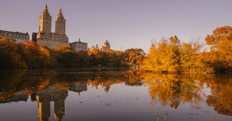 Stunning autumn view of Central Park with skyline reflection on the calm reservoir water.