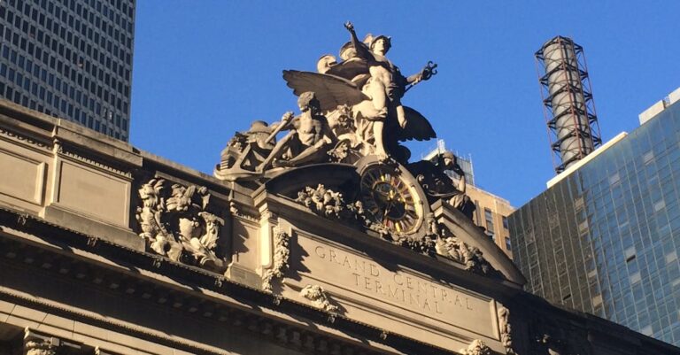 Historic facade of Grand Central Terminal with sculptures against a clear blue sky.