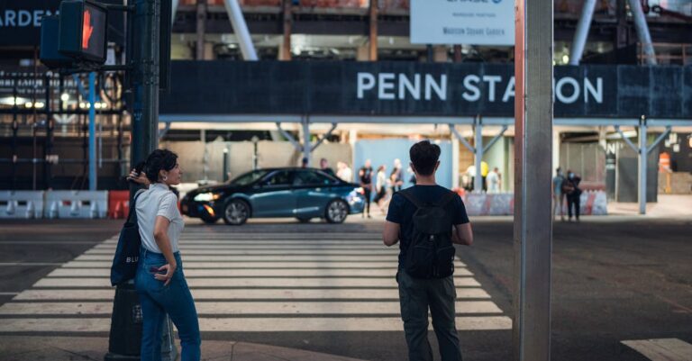 Two people wait at a pedestrian crossing near Penn Station in New York City, capturing urban life.