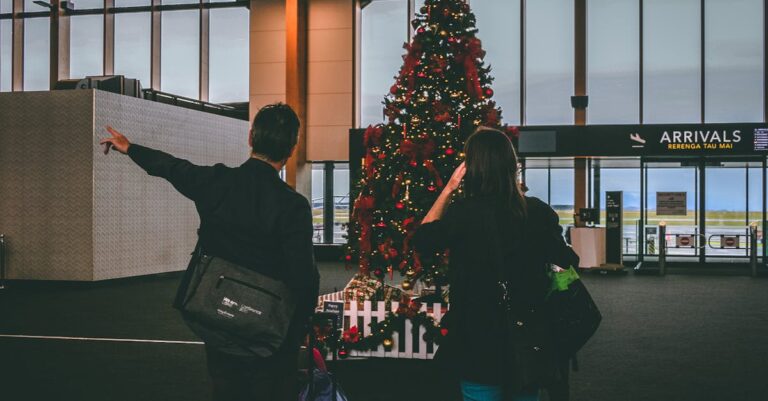 Young couple observes Christmas tree inside airport terminal.