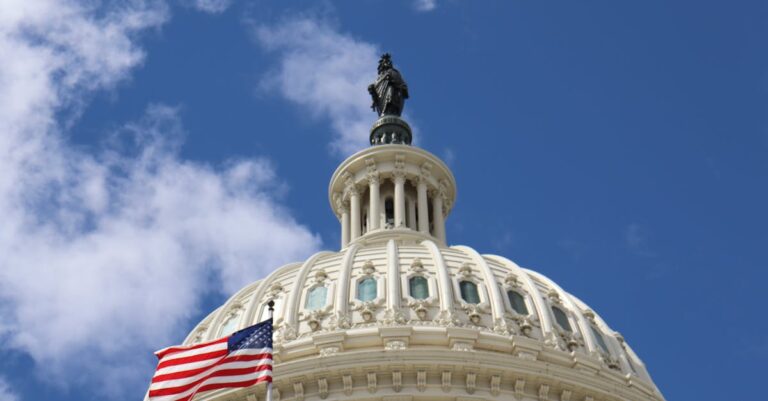 Capture of the U.S. Capitol dome with an American flag waving against a blue sky in Washington, D.C.