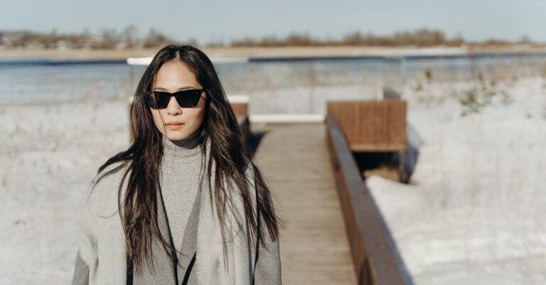 Asian woman in winter attire standing on a snowy boardwalk, enjoying the serene countryside view.