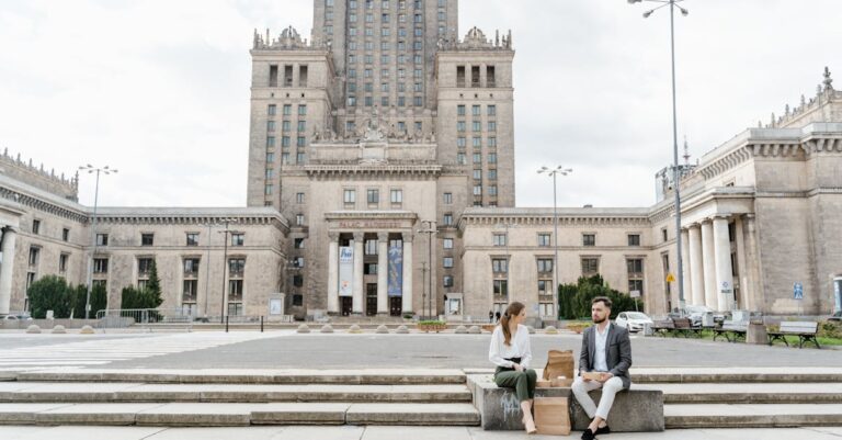 Two colleagues enjoy lunch on steps of Warsaw's Palace of Culture and Science.