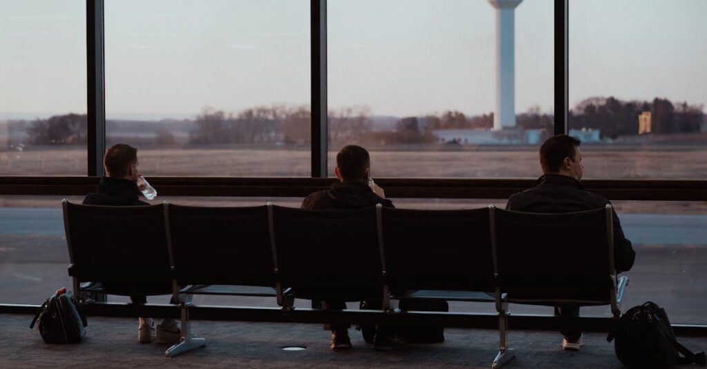 People sitting in airport terminal, watching runway scenes through large windows.