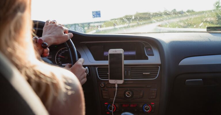 View from behind a woman driving a car on a sunny day with a phone mounted on the dashboard.