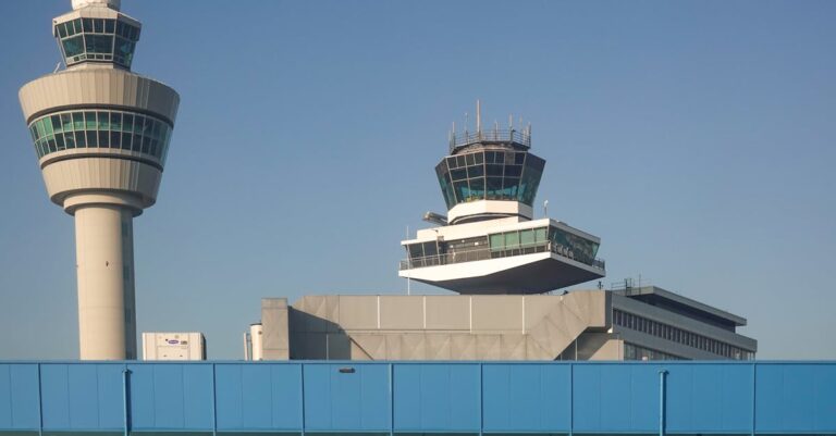 View of air traffic control towers at Amsterdam Schiphol Airport under clear blue sky.