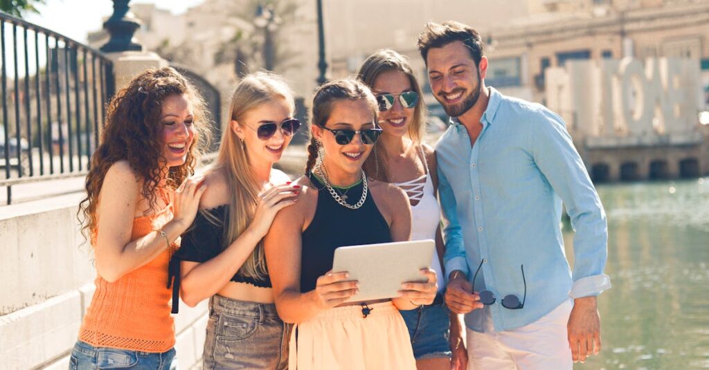 Five friends laughing together by the waterfront in Malta, enjoying a sunny day and sharing a tablet.