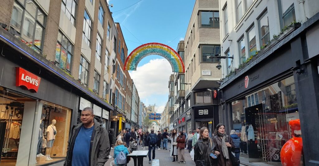 A bustling urban street with shops and a colorful rainbow decoration under a bright blue sky.
