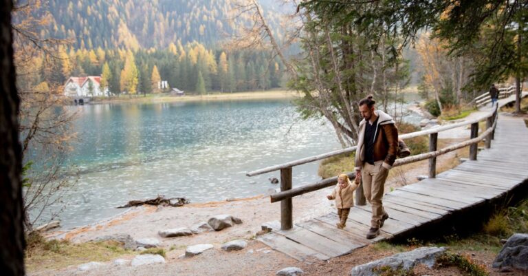 A father and child walk by a picturesque lake surrounded by autumn trees, capturing a moment of togetherness and adventure.