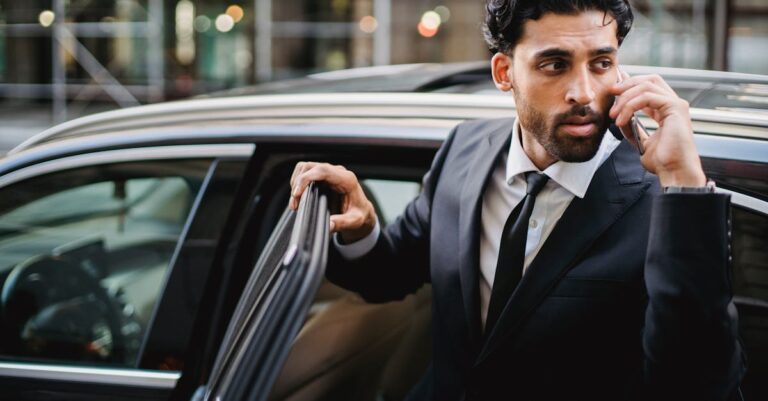 Confident businessman in a suit stepping out of a car while talking on the phone.
