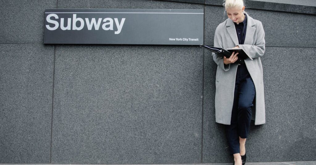 Full body smiling young businesswoman in formal clothes and coat reading documents and standing near subway station entrance