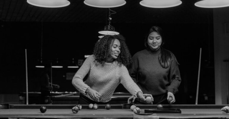 Two women playing billiards in a modern nightclub setting, enjoying leisure time.