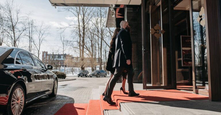 A man and woman elegantly dressed enter a luxury hotel, walking on a red carpet.