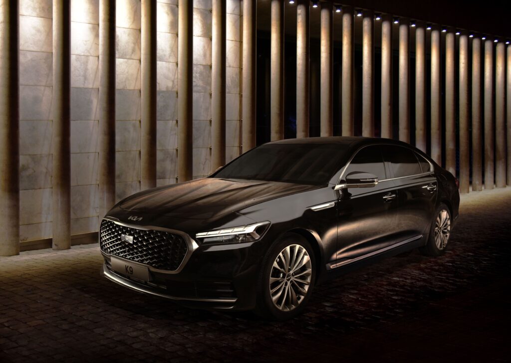 Sleek black K9 sedan parked elegantly against a lit modern architecture backdrop at night.
