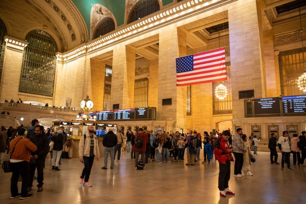 Travelers arriving beneath the flag inside Grand Central Terminal in New York City