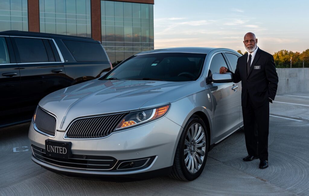 Professional chauffeur in a suit standing beside a luxury car